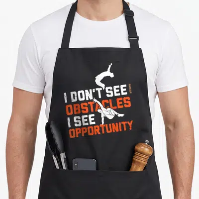 Free running parkour apron - Stacked I DON'T SEE OBSTACLES I SEE OPPORTUNITY text with two white leaping athlete — shown on a black cotton canvas apron against a white background