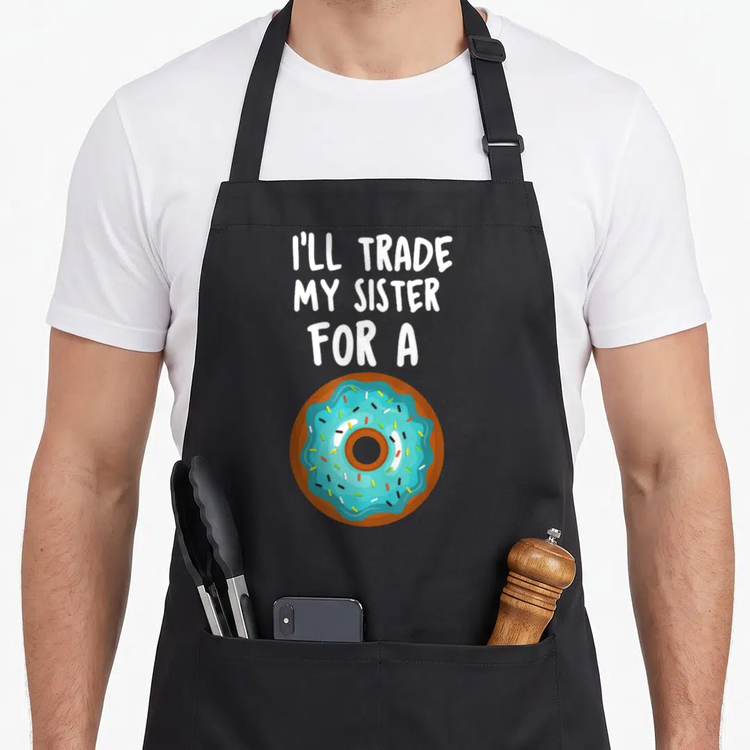 Ill donut apron - Cartoon blue frosted donut with sprinkles below white text reading I'll Trade My Sister — shown on a black cotton canvas apron against a white background