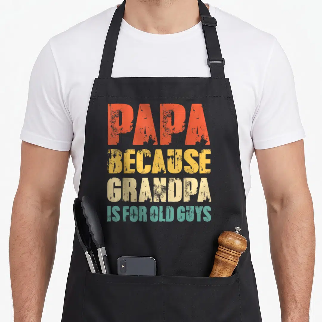 Vintage papa grandpa apron - Stacked PAPA BECAUSE GRANDPA IS FOR OLD GUYS text in orange yellow beige teal — shown on a black cotton canvas apron against a white background