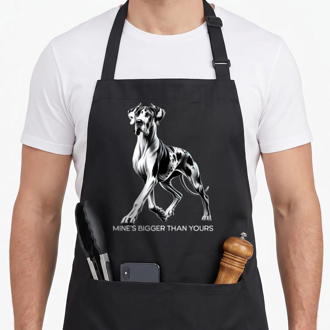 Mine great dogs apron - Realistic black and white Great Dane standing above text Mine's Bigger Than Yours — shown on a black cotton canvas apron against a white background