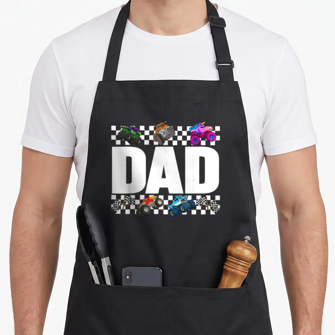 Family crew truck apron - DAD text with three monster trucks above and two below plus four checkered flags in cartoon — shown on a black cotton canvas apron against a white background