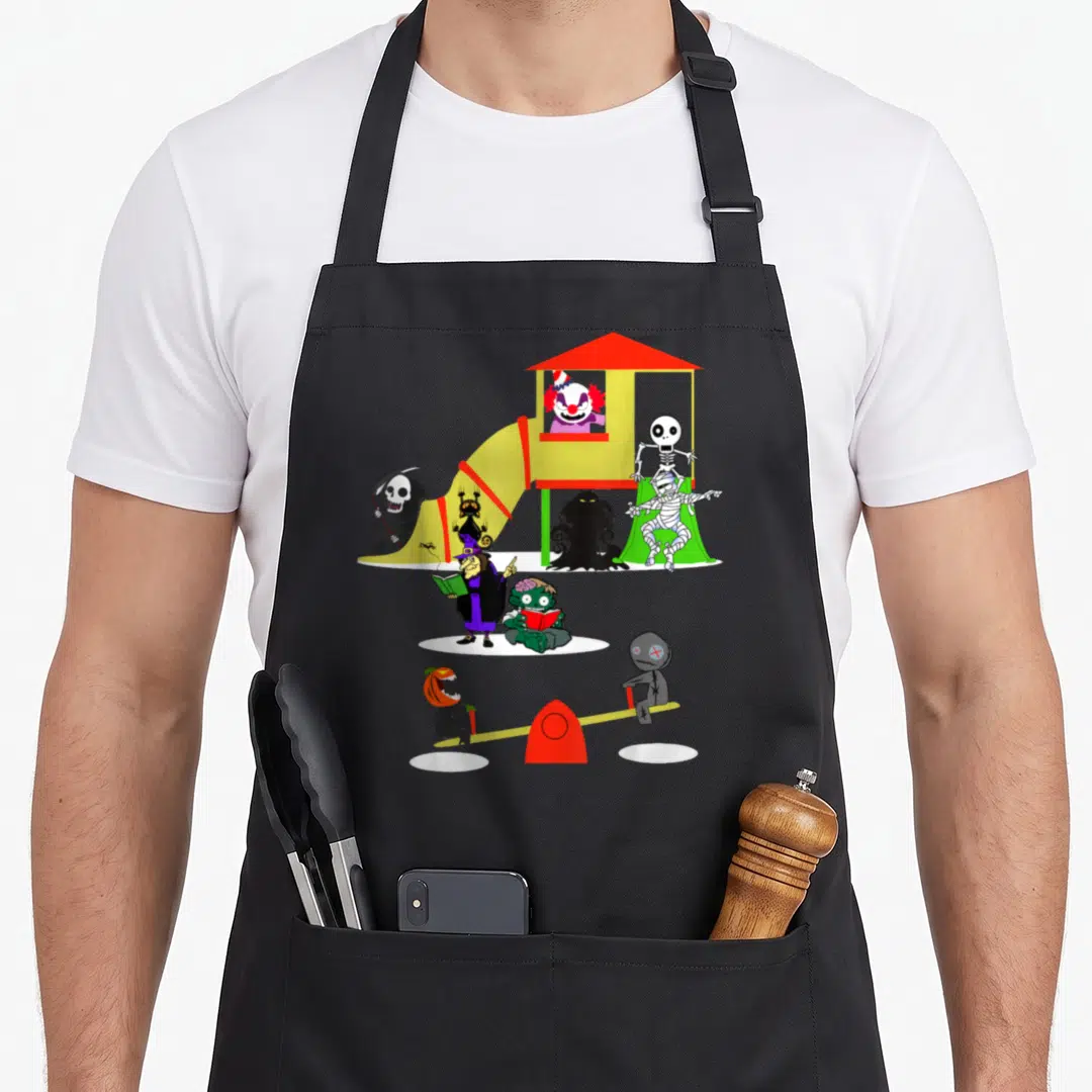 Icon horror movie apron - Cartoon monsters including a clown, skeleton, mummy, and witch playing on a colorful — shown on a black cotton canvas apron against a white background