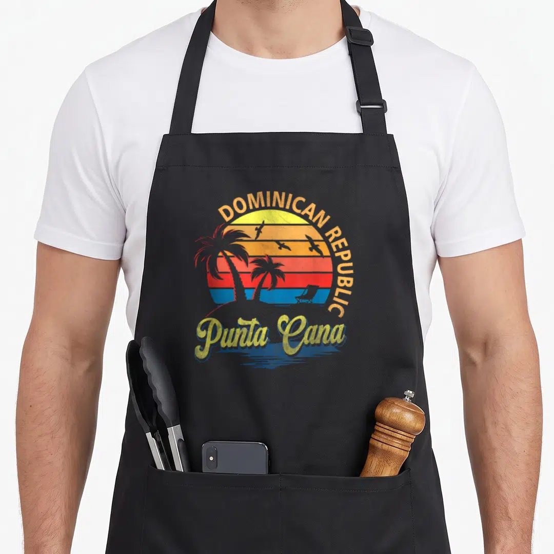 Sunset dominican apron - Retro sunset with DOMINICAN REPUBLIC text, Punta Cana script, and palm tree silhouettes — shown on a black cotton canvas apron against a white background