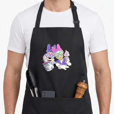 Cool daisy apron - Minnie and Daisy wearing heart sunglasses holding a drink and ice cream in purple pink and teal — shown on a black cotton canvas apron against a white background