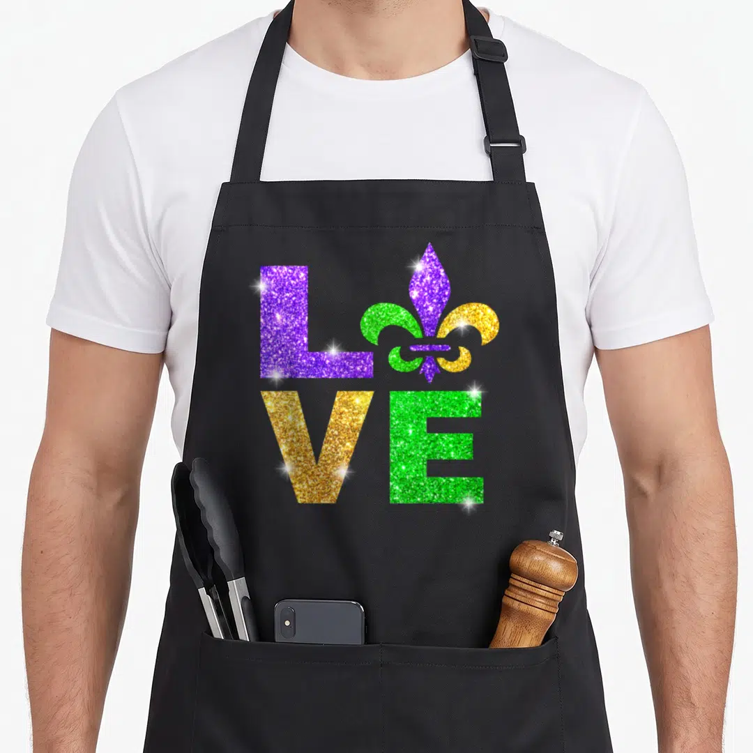 Fleur mardi gras aprons - LOVE text with fleur-de-lis symbol in purple gold and green square grid — shown on a black cotton canvas apron against a white background