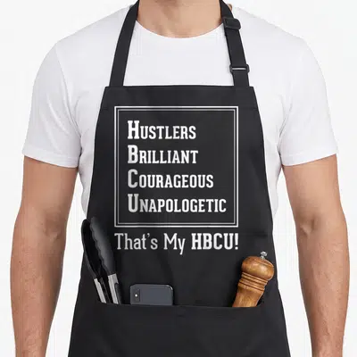 Proud unapologetic apron - White text HUSTLERS BRILLIANT COURAGEOUS UNAPOLOGETIC That's My HBCU! on black background — shown on a black cotton canvas apron against a white background