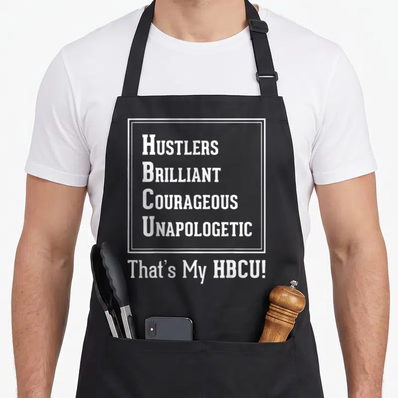 Proud unapologetic apron - White text HUSTLERS BRILLIANT COURAGEOUS UNAPOLOGETIC That's My HBCU! on black background — shown on a black cotton canvas apron against a white background
