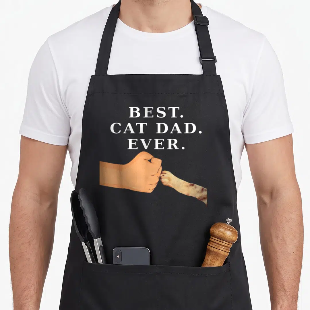 Father kitty cat apron - White text reading BEST CAT DAD EVER above a human fist bumping a tan and brown cat paw — shown on a black cotton canvas apron against a white background