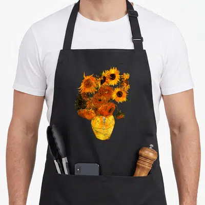 Gogh sunflower apron - Realistic cluster of sunflowers in yellow vase with orange yellow and green tones — shown on a black cotton canvas apron against a white background