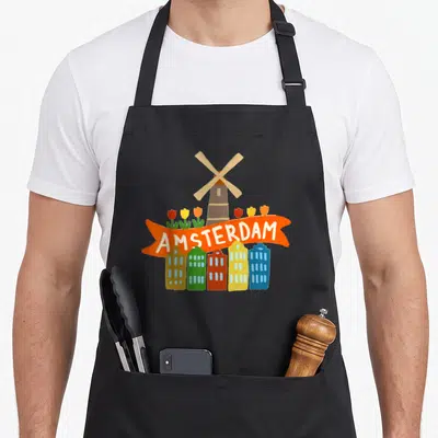 Amsterdam tulip apron - Cartoon windmill, tulips, five colorful houses, and orange AMSTERDAM banner — shown on a black cotton canvas apron against a white background