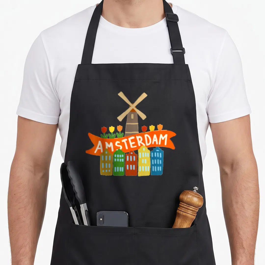 Amsterdam tulip apron - Cartoon windmill, tulips, five colorful houses, and orange AMSTERDAM banner — shown on a black cotton canvas apron against a white background