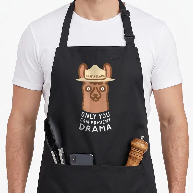 Original glamping apron - Cartoon brown llama head with hat reading Drama Llama and white text Only You Can Prevent — shown on a black cotton canvas apron against a white background