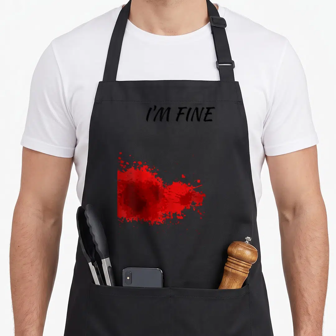 Fine bloody apron - I'M FINE text above irregular red splatter on black background — shown on a black cotton canvas apron against a white background