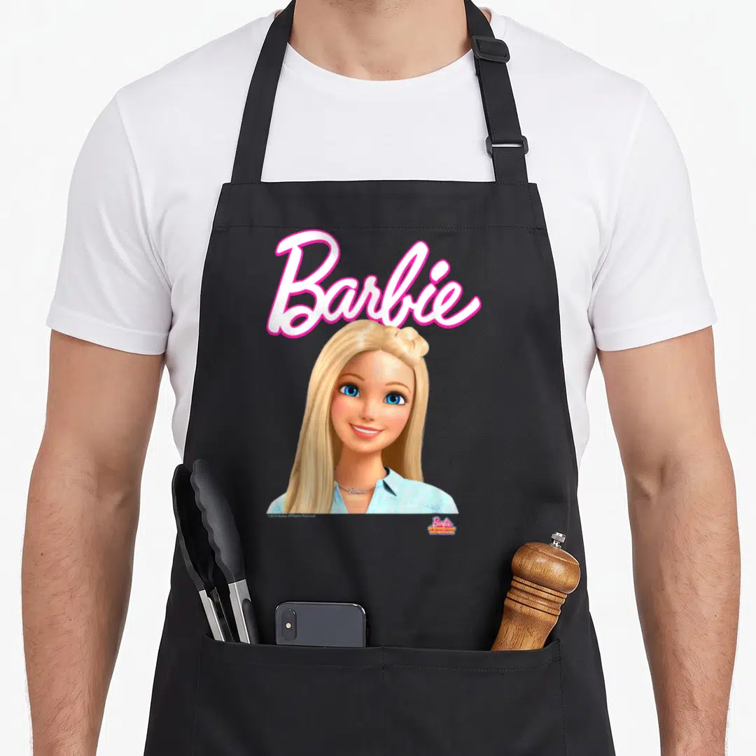 Dreamhouse little miss apron - Pink Barbie script above a blonde woman in a blue shirt with blue eyes — shown on a black cotton canvas apron against a white background