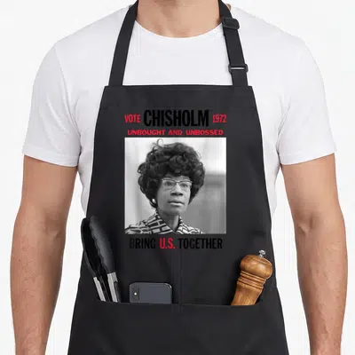 History senator apron - VOTE CHISHOLM 1972 text above and below a black and white photo of a woman in red and white — shown on a black cotton canvas apron against a white background