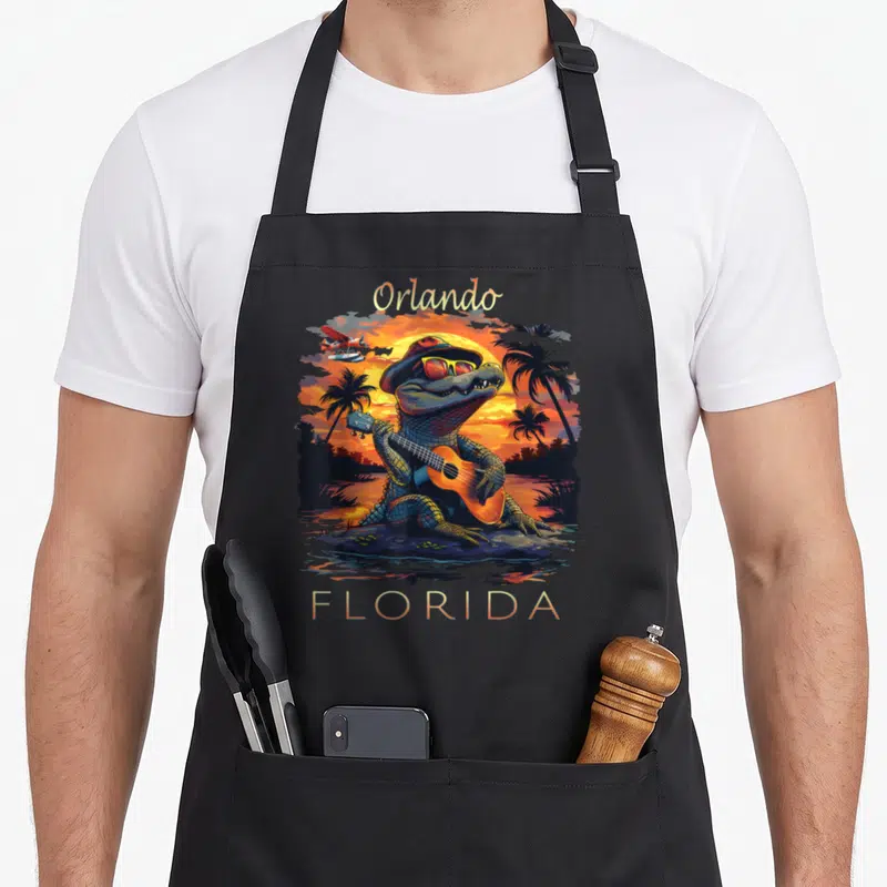 Orlando vacation alligator florida apron - Cartoon alligator playing guitar at sunset with Orlando Florida text — shown on a black cotton canvas apron against a white background