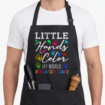 Hand nurse apron - Stacked text Little Hands Color My World Pediatric Care with multi-colored handprints and splatters — shown on a black cotton canvas apron against a white background