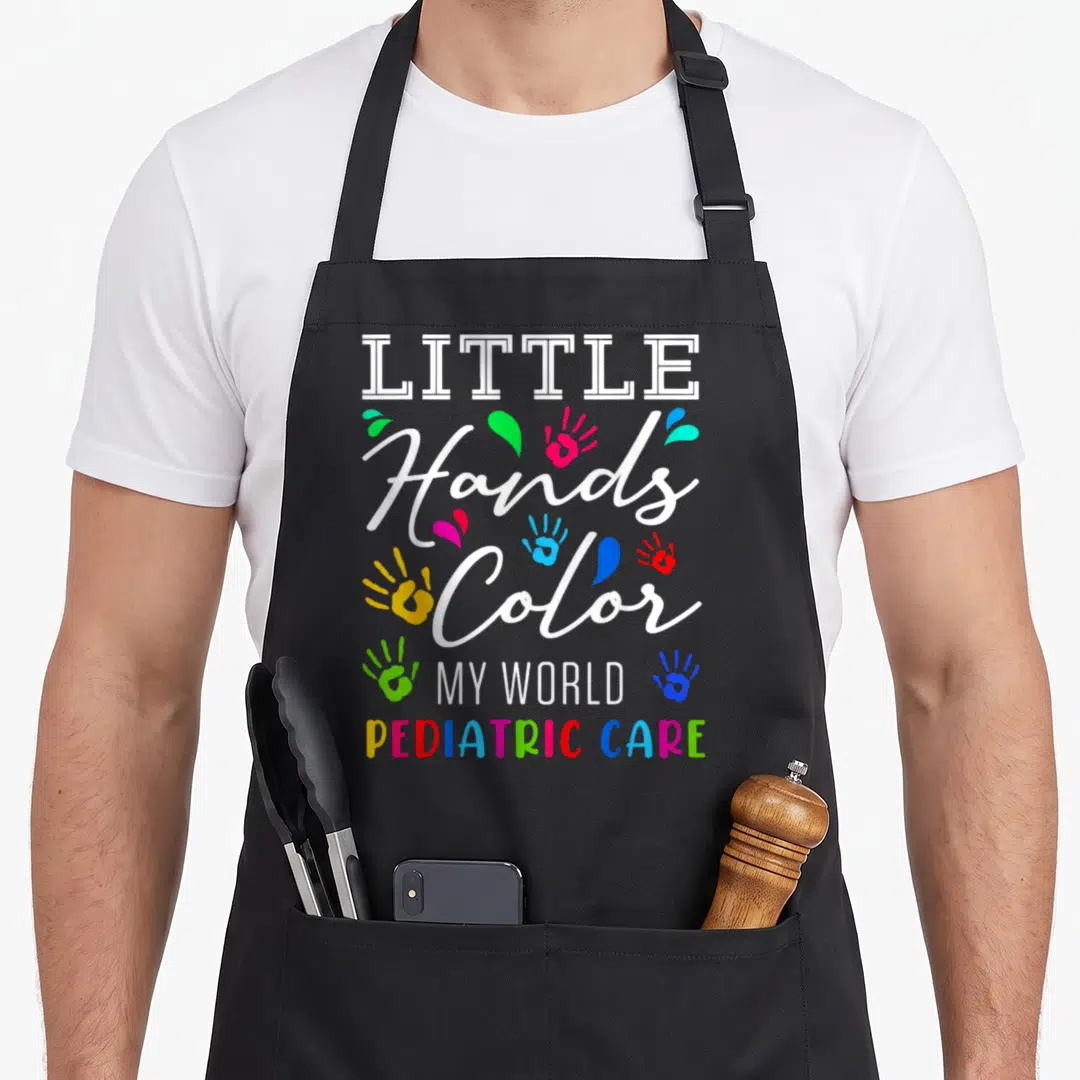 Hand nurse apron - Stacked text Little Hands Color My World Pediatric Care with multi-colored handprints and splatters — shown on a black cotton canvas apron against a white background