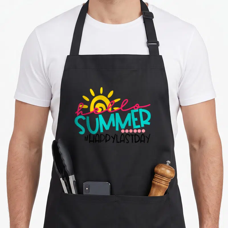 School student teacher apron - Yellow sun with pink hello and turquoise SUMMER text above pink dots and black hashtag — shown on a black cotton canvas apron against a white background