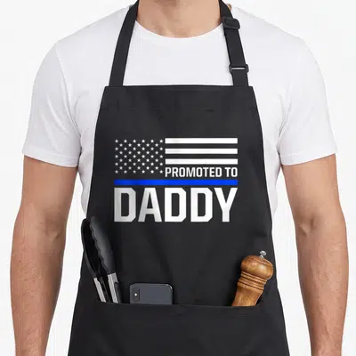 Police daddy apron - White flag graphic with Promoted To Daddy text and thin blue line — shown on a black cotton canvas apron against a white background