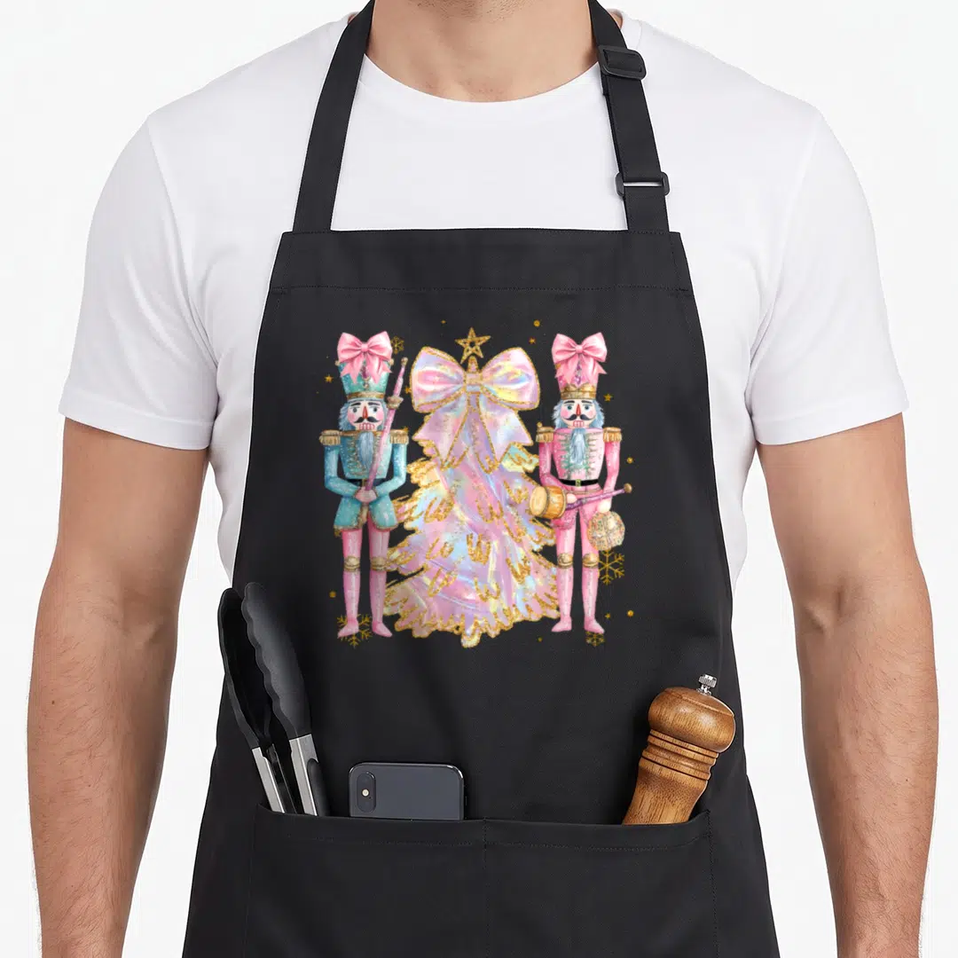 Nutcracker christmas tree apron - Pink bow Christmas tree flanked by blue and pink nutcracker soldiers with gold accents — shown on a black cotton canvas apron against a white background