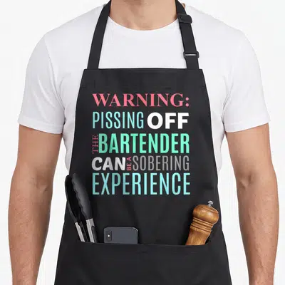Sarcastic bartender apron - Stacked text reading WARNING PISSING OFF THE BARTENDER CAN BE A SOBERING EXPERIENCE in pink — shown on a black cotton canvas apron against a white background