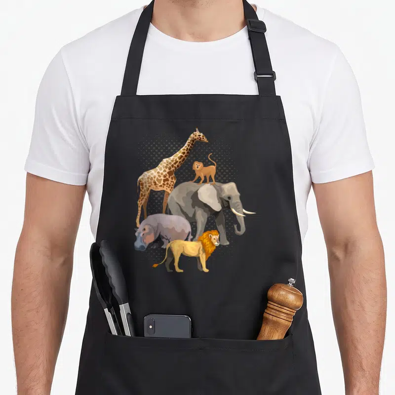 Safari african apron - Cartoon giraffe, elephant, monkey, lion, and hippo in grey orange brown yellow with halftone dots — shown on a black cotton canvas apron against a white background