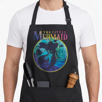 Poster mermaid apron - Retro circular print with THE LITTLE MERMAID text, mermaid silhouette, castle, and fish in blue — shown on a black cotton canvas apron against a white background