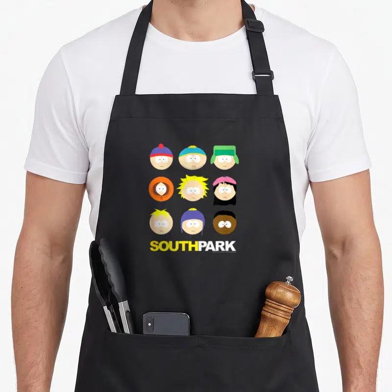 Grid face apron - Nine cartoon heads in a 3x3 grid above yellow and white SOUTH PARK text — shown on a black cotton canvas apron against a white background