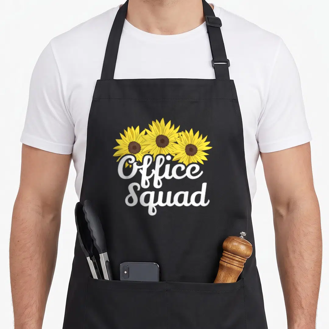 Office sunflower apron - Three yellow sunflowers with brown centers above white Office Squad script text — shown on a black cotton canvas apron against a white background