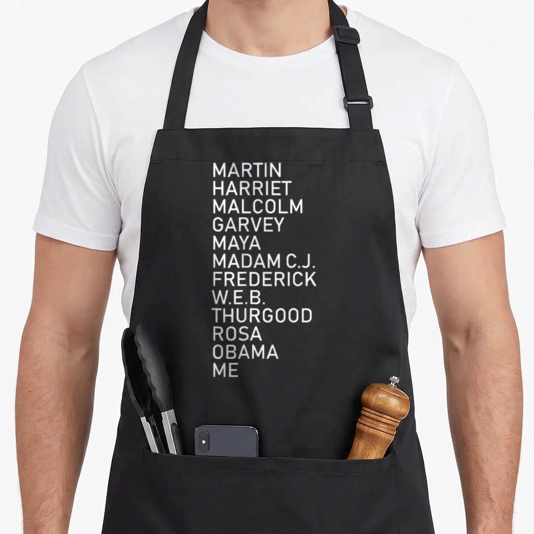 History violinist apron - Vertical white text listing Martin Harriet Malcolm Garvey Maya Madam C.J. Frederick W.E.B — shown on a black cotton canvas apron against a white background