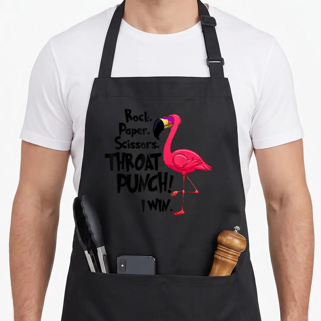 Throat paper apron - Pink flamingo standing next to black text Rock Paper Scissors Throat Punch I Win — shown on a black cotton canvas apron against a white background
