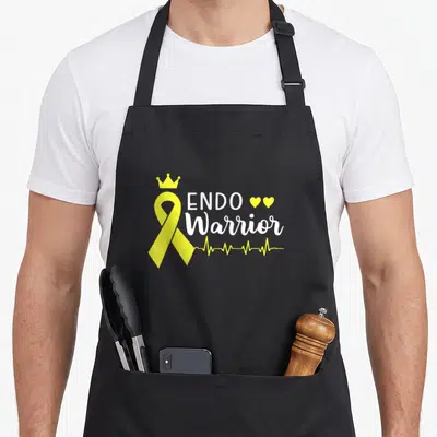 Cancer endometriosis awareness apron - Yellow ribbon with crown, ENDO Warrior text, two hearts, and heartbeat line — shown on a black cotton canvas apron against a white background