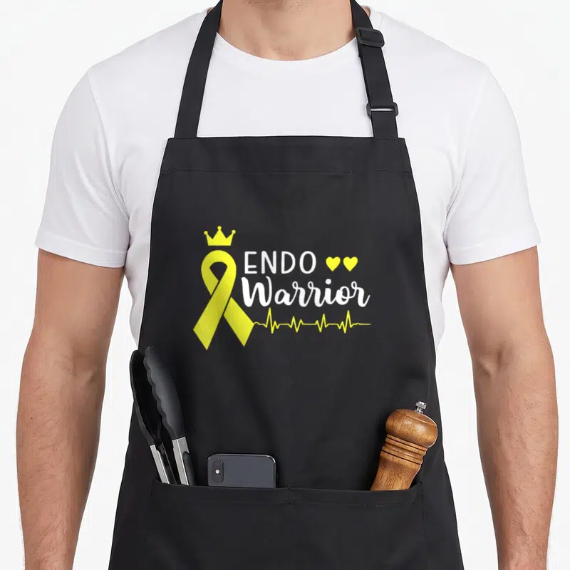 Cancer endometriosis awareness apron - Yellow ribbon with crown, ENDO Warrior text, two hearts, and heartbeat line — shown on a black cotton canvas apron against a white background