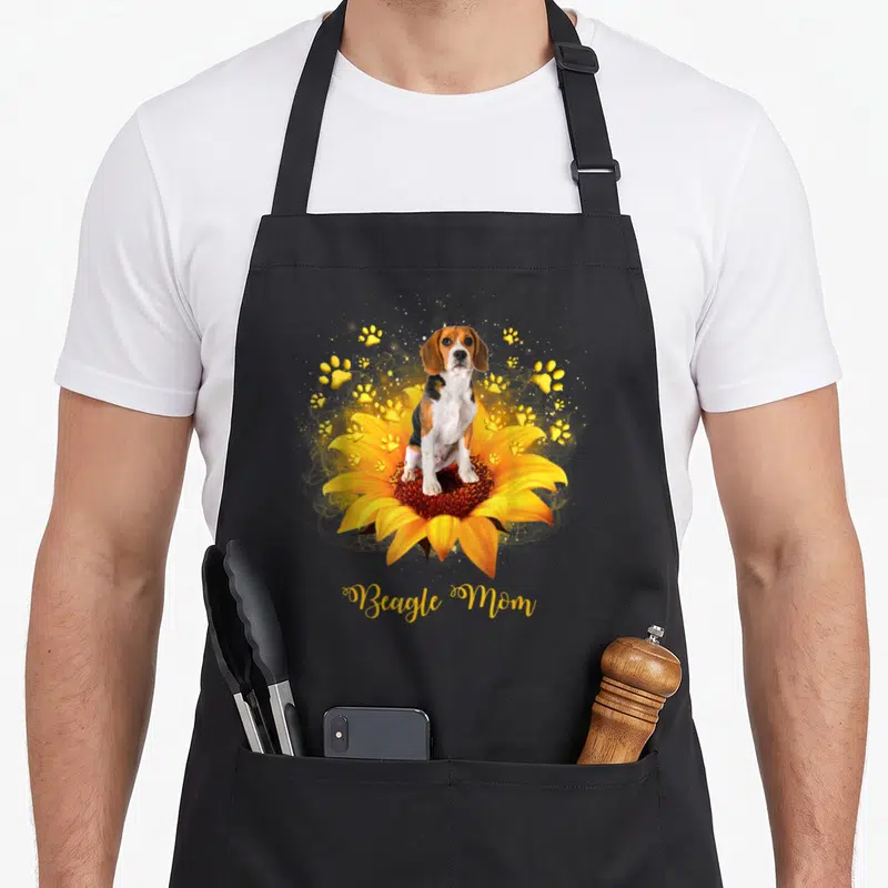 Beagle mother's day aprons - Photo of a beagle sitting in a sunflower surrounded by yellow paw prints and Beagle Mom — shown on a black cotton canvas apron against a white background