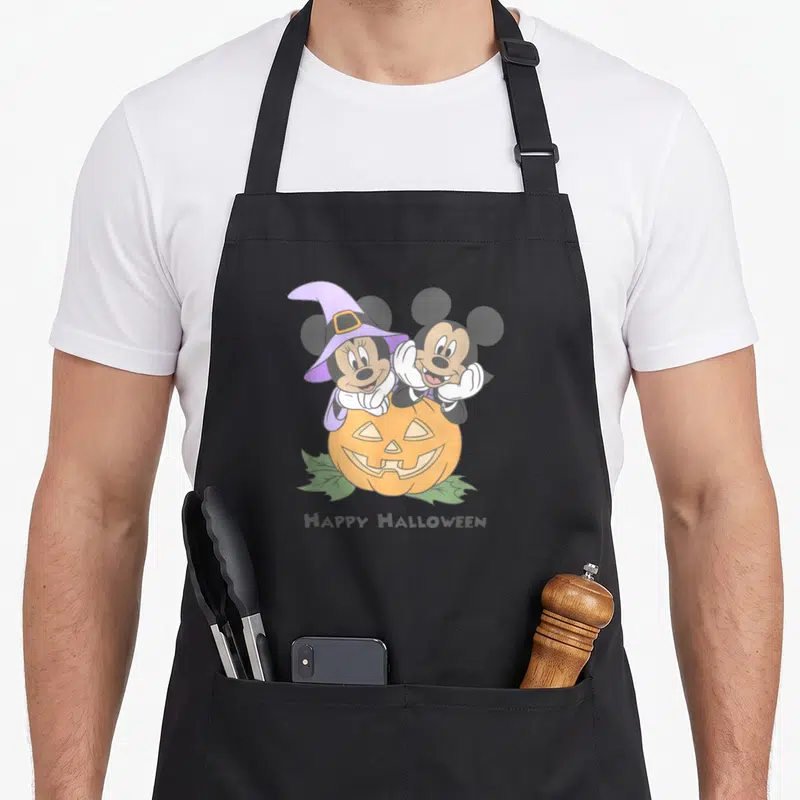 Friend pumpkin halloween kitchen aprons - Mickey and Minnie Mouse leaning over orange pumpkin with HAPPY HALLOWEEN text — shown on a black cotton canvas apron against a white background