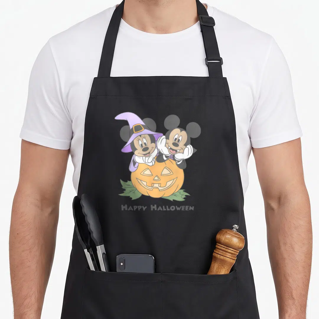 Friend pumpkin halloween kitchen aprons - Mickey and Minnie Mouse leaning over orange pumpkin with HAPPY HALLOWEEN text — shown on a black cotton canvas apron against a white background
