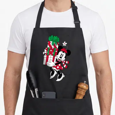 General fun apron - Cartoon Minnie Mouse in winter clothes and skates holding three red and white wrapped presents — shown on a black cotton canvas apron against a white background