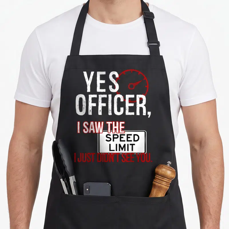 Driver police apron - Red speedometer next to white and red text about speed limit and officers — shown on a black cotton canvas apron against a white background