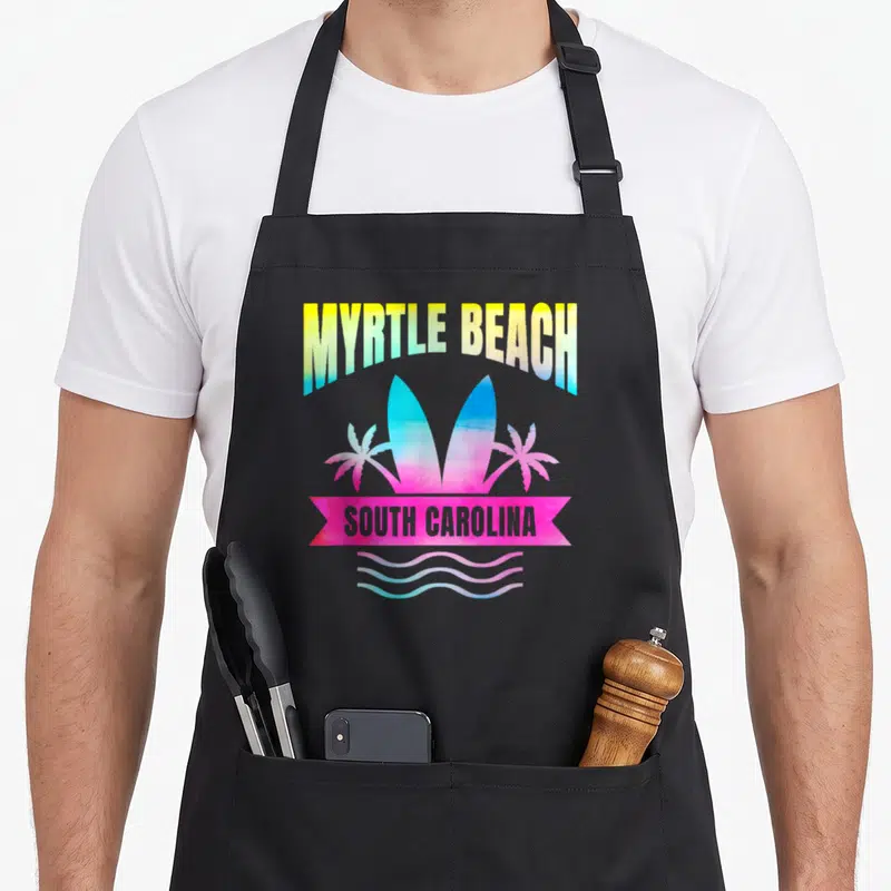 Myrtle beach family apron - Arched MYRTLE BEACH text above two surfboards, pink ribbon with SOUTH CAROLINA — shown on a black cotton canvas apron against a white background