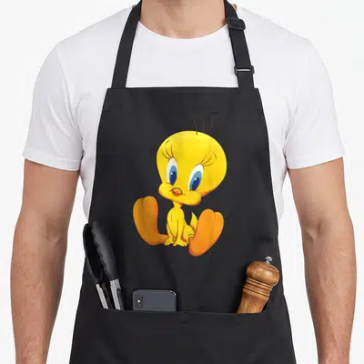 Tweety crazy bunny man apron - Yellow cartoon bird sitting with orange feet and large blue eyes — shown on a black cotton canvas apron against a white background