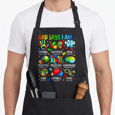 Kind god says i am apron - Colorful puzzle pieces, boxing gloves, brain, and scripture verses arranged in a grid layout — shown on a black cotton canvas apron against a white background