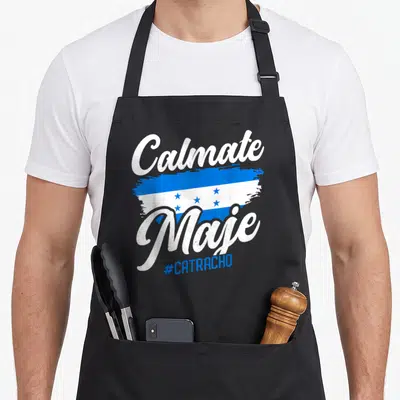 Baleada honduran apron - Calmate Maje text with blue white brushstroke flag and #CATRACHO hashtag — shown on a black cotton canvas apron against a white background