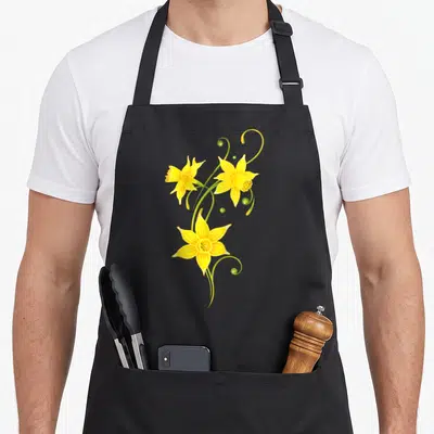 Daffodil spring apron - Three yellow daffodils with curving green stems and small berries on black fabric — shown on a black cotton canvas apron against a white background