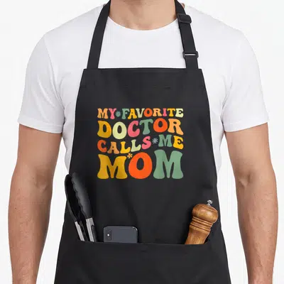 Call groovy mother's day aprons - Bubbly text My Favorite Doctor Calls Me Mom in orange yellow green red and blue — shown on a black cotton canvas apron against a white background