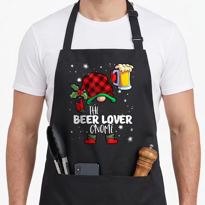 Beer buffalo plaid christmas apron - Cartoon gnome in red plaid hat holding holly and beer mug with stacked white text — shown on a black cotton canvas apron against a white background