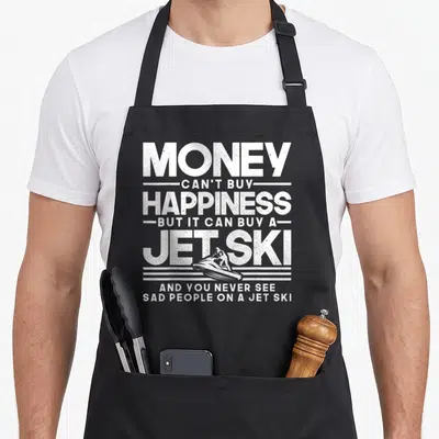 Jet jetski apron - White distressed text reading money cant buy happiness but it can buy a jet ski with a rider — shown on a black cotton canvas apron against a white background