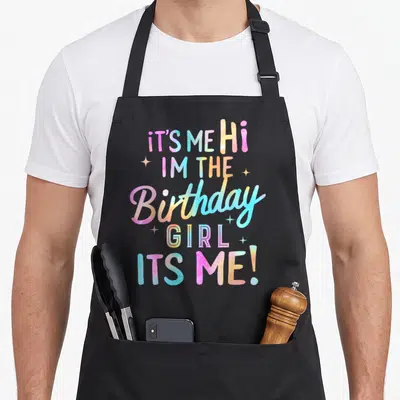 Occasion birthday apron - Tie-dye text IT'S ME Hi IM THE Birthday GIRL with white sparkles — shown on a black cotton canvas apron against a white background