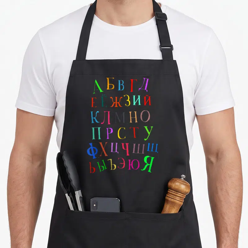 Funny alphabet russian apron - Colorful Cyrillic alphabet letters stacked in six rows printed on grey fabric — shown on a black cotton canvas apron against a white background