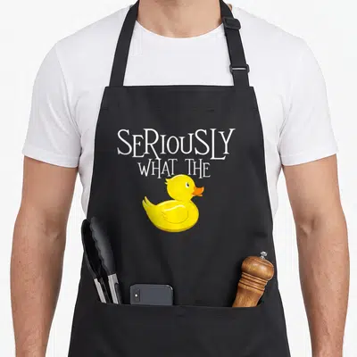 Seriously duck apron - Stacked white text SERIOUSLY WHAT THE above a yellow rubber duck with an orange beak — shown on a black cotton canvas apron against a white background